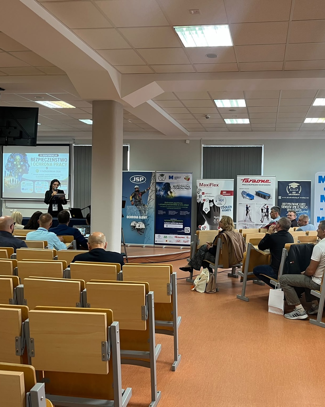 Uczestnicy IV Konferencji Bezpieczeństwo i Ochrona Pracy w auli Uniwersytetu WSB Merito Łódź; wśród ekspozycji widoczny roll-up Faraone.